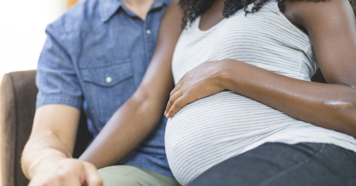 Pregnant couple sits on couch together. Pregnant couple sits on couch together.